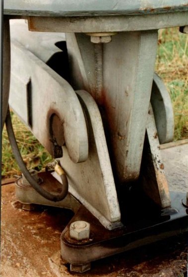 Close-up of the gin-pole attachment at the tower pivot, showing the hinge plates, pin and bolted steel fittings at the base