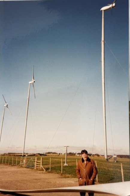 Steve standing in front of a row of Carter two-blade turbines on guyed tilt-down towers, with a tower rest stand visible behind