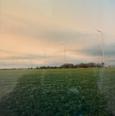 The row of Carter turbines on their guyed towers across a green field at Great Orton, Cumbria, at dusk