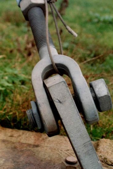 Close-up of a guy cable ground attachment: the cable swaged to a threaded turnbuckle and shackle bolted to the ground anchor