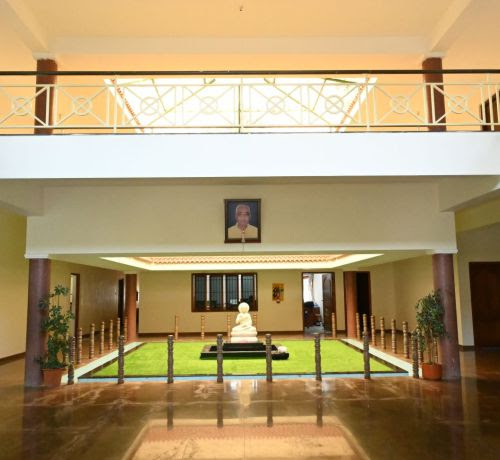 Interior atrium of the joint venture offices in India — a double-height lobby with a first-floor balustrade, a framed portrait, a small statue and lawn
