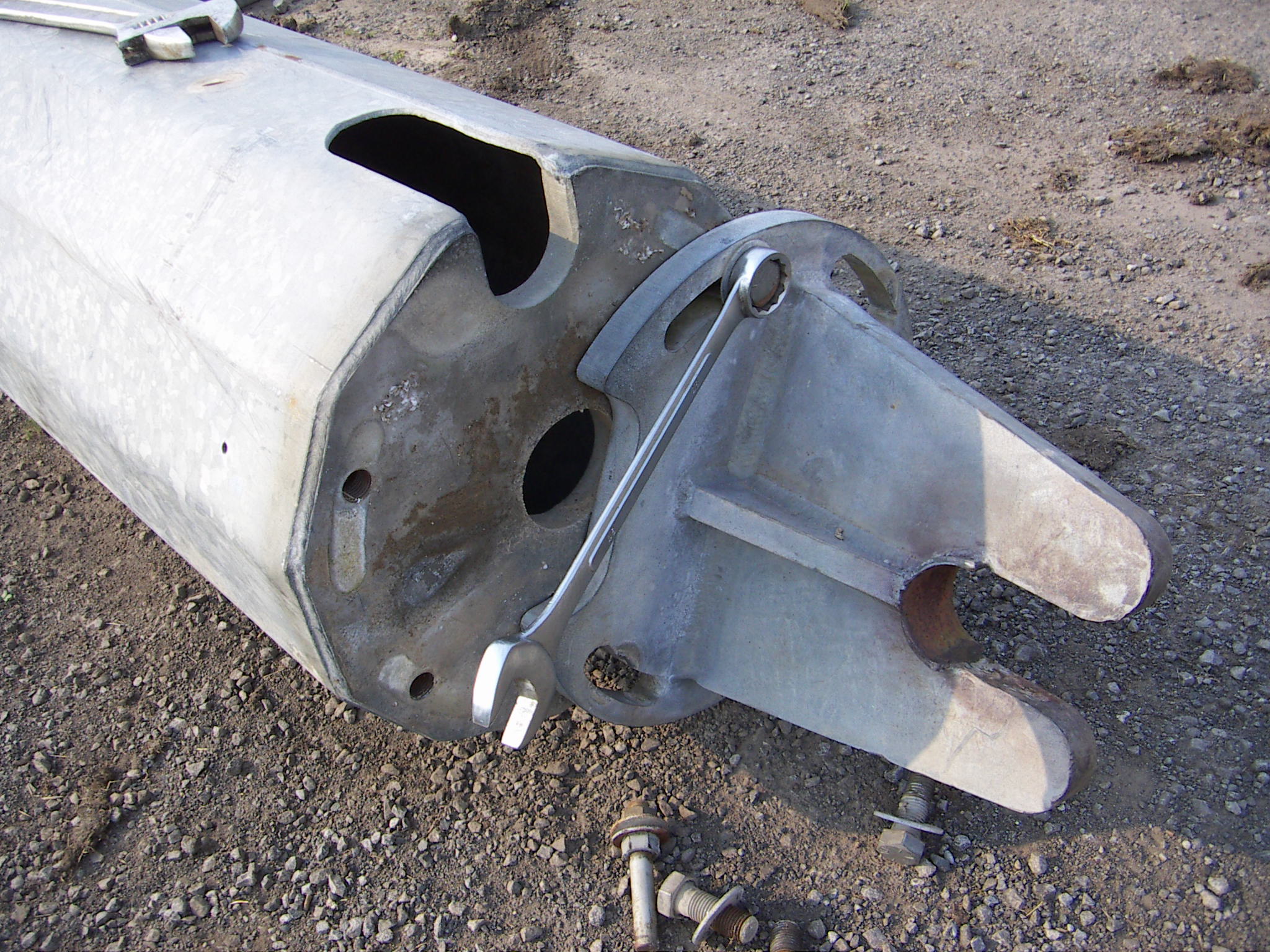 Close-up of the tower base end fitting on the ground, showing the cast pivot bracket, bolt holes and spanners during assembly
