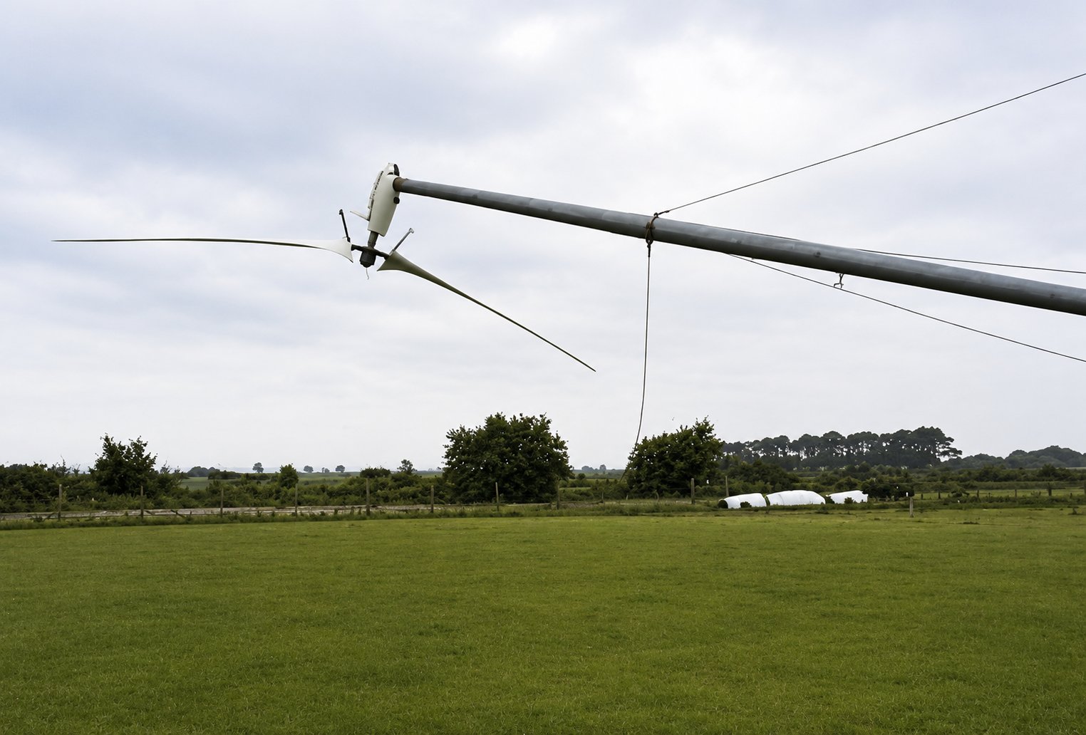 A Carter two-blade turbine on its guyed tower at Great Orton, Cumbria, tilted down to near ground level for service, with the rotor low over the grass