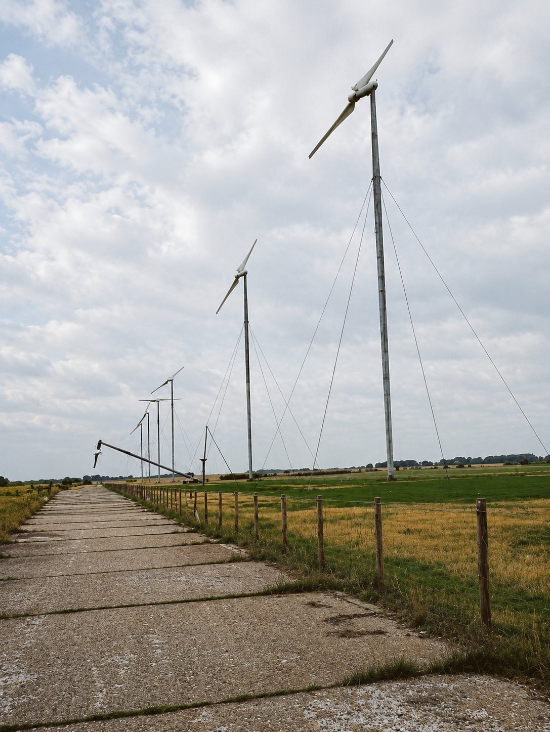 A row of Carter two-blade turbines on guyed tilt-down towers in an open field, one lowered for service