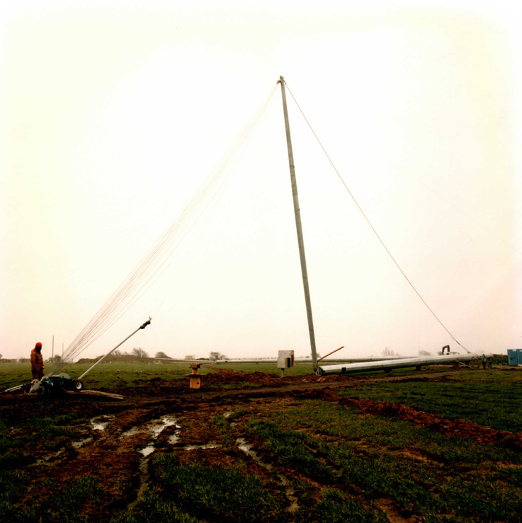 Gin pole rigged and lifting tackle spread — the tower lies horizontal on its trestle, ready for the pull.